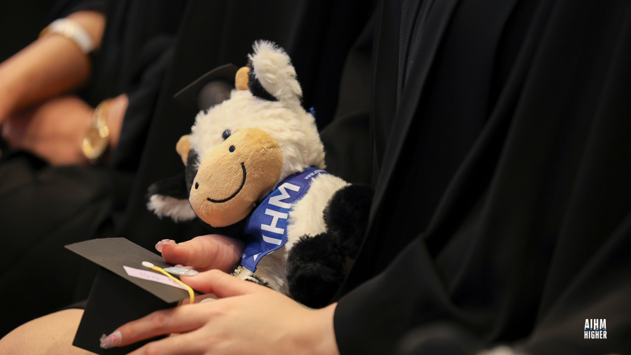 A graduate holds a AIHMY cow wearing an AIHM ribbon and a miniature graduation cap, symbolising celebration and achievement during the AIHM Graduation Ceremony 2025.