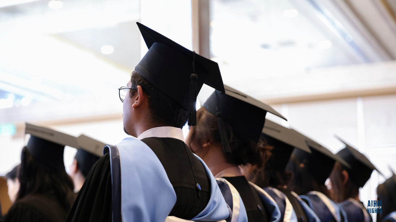 Graduates in black gowns and caps sit attentively during the AIHM Graduation Ceremony 2025. The soft lighting reflects a moment of pride and anticipation.