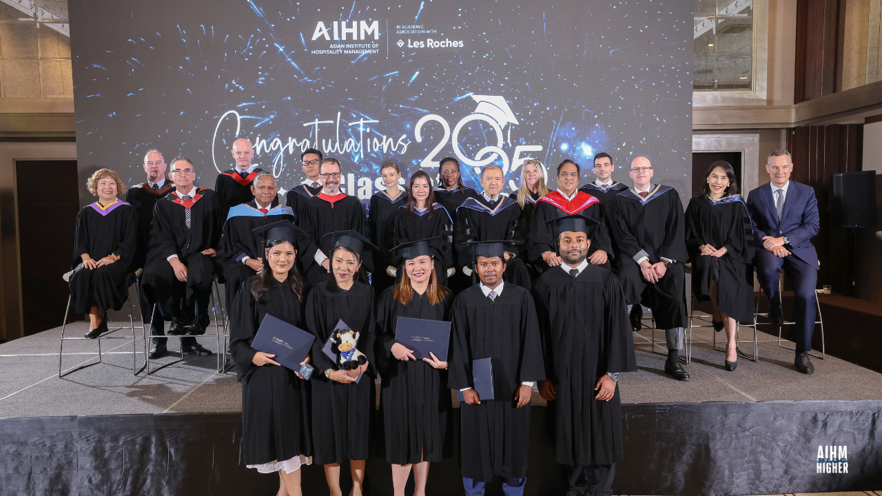 A group of CIHA3 graduates pose with their certificates in front of seated faculty members. The festive backdrop featuring fireworks celebrates the Class of 2025.
