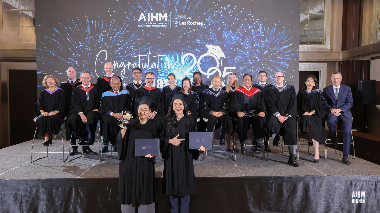 CIHA4 graduates proudly hold their certificates while posing with AIHM faculty and management team on stage. The backdrop displays “Congratulations Class of 2025” with blue fireworks graphics.