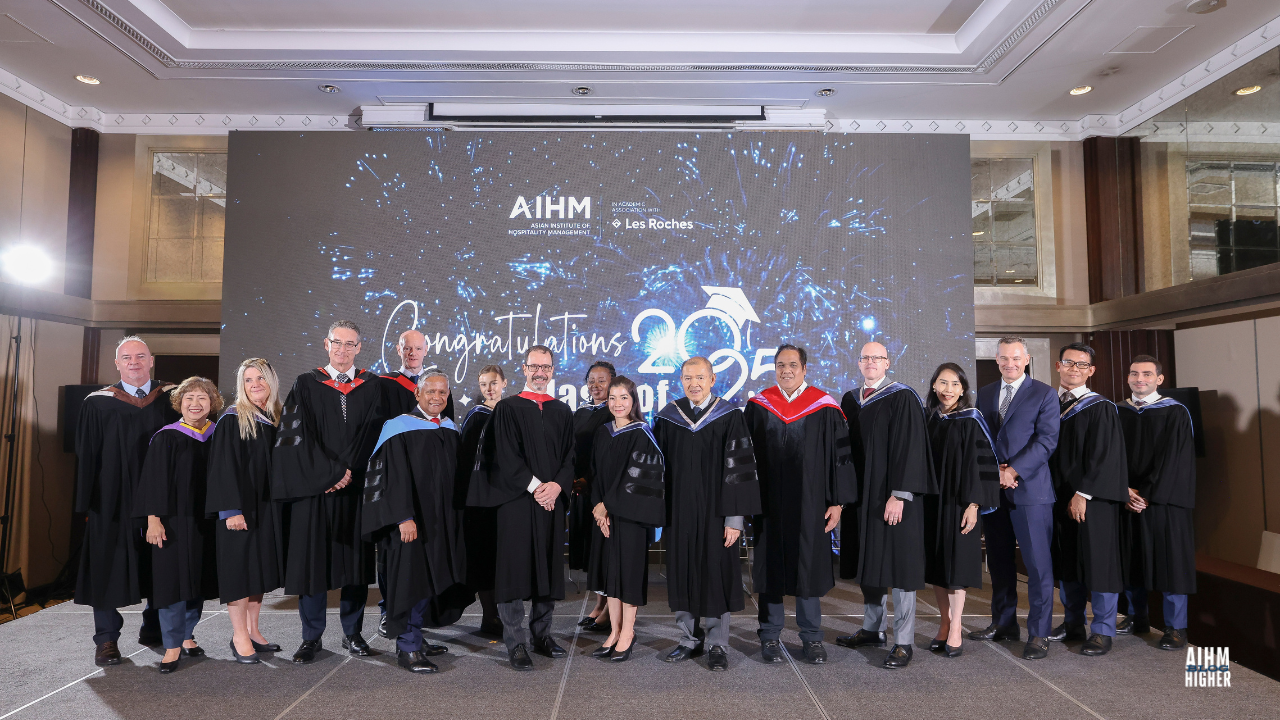 AIHM academic team and leadership Board of Trusty pose together on stage during the Graduation Ceremony 2025. The group stands in front of a screen displaying “Congratulations Class of 2025” with celebratory blue fireworks graphics.